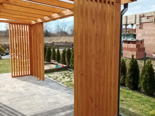 Drewniana altana z pionowymi lamelami i zadaszeniem, posadzka z kostki