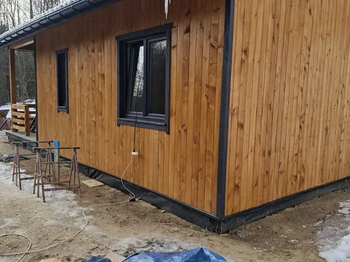 Narożnik domu drewnianego z pionową elewacją, ciemnym oknem i rynną
