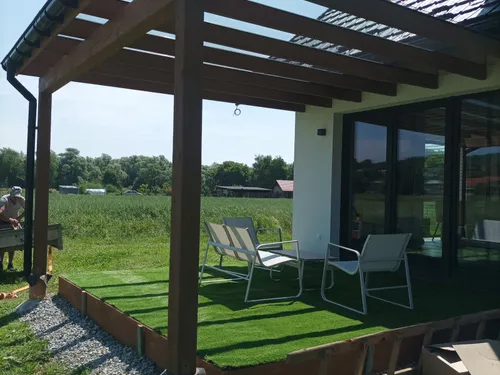 Pergola z belkami z ciemnego drewna nad tarasem z meblami ogrodowymi